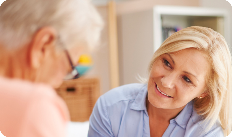 A middle-aged woman is having a conversation with an older woman, explaining what to expect during a hearing test from Beltone.
