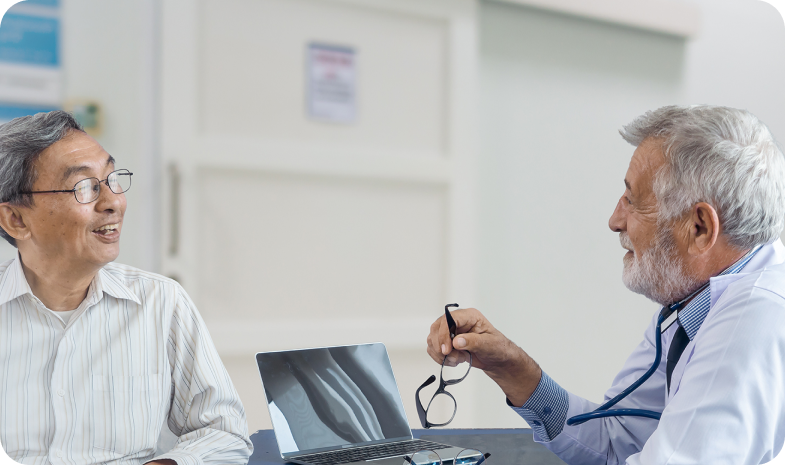 An older male audiologist meets with a male patient, discussing hearing aid options during a hearing test. 