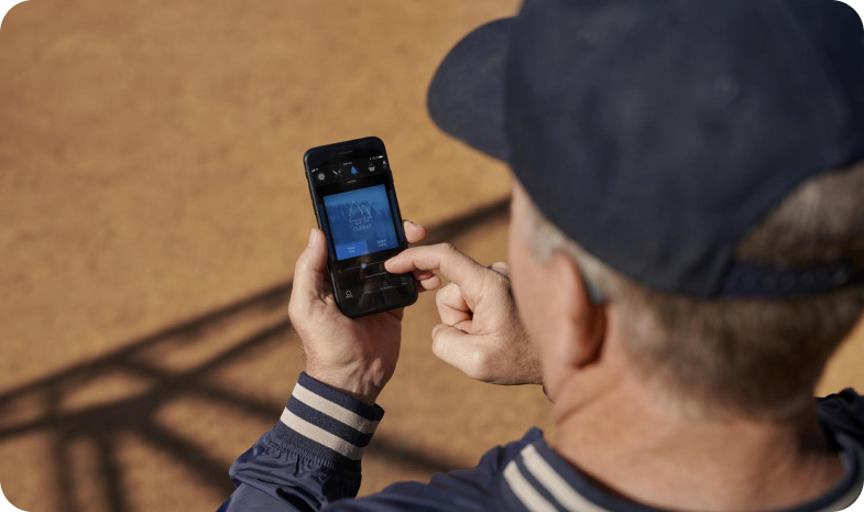 An older man uses the Beltone hearing aid app on his phone. He's visibly wearing a hearing aid behind his ear.