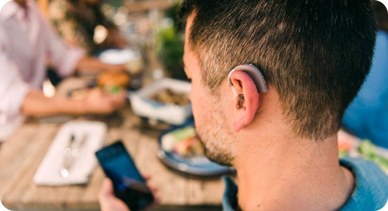 An image shows the back of a man's head as he looks at this smartphone. He's wearing a Beltone hearing aid behind his left ear.