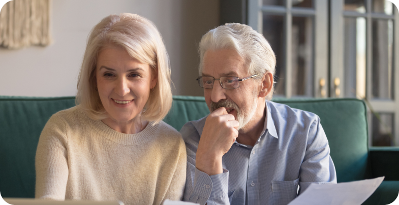 An older man and woman couple are pictured sitting on a couch, reviewing hearing aid payment options from Beltone NE.