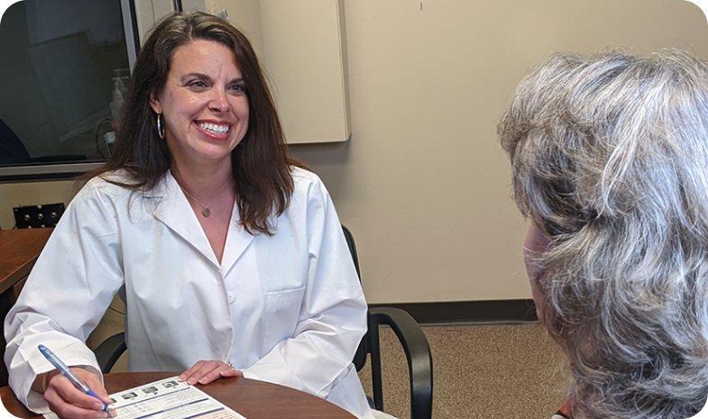 A female Beltone hearing specialist speaks with an older woman about her hearing test results. The doctor is smiling while filling out paperwork.