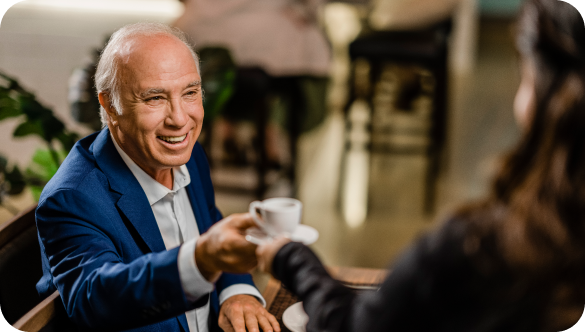 An older man smiles as he accepts a cup of coffee from a woman.