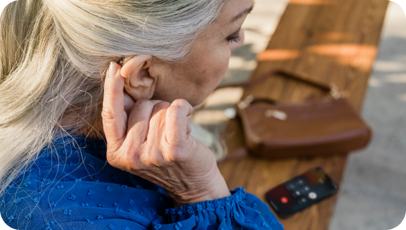 A older woman adjusts her hearing aid, which is positioned behind her ear.
