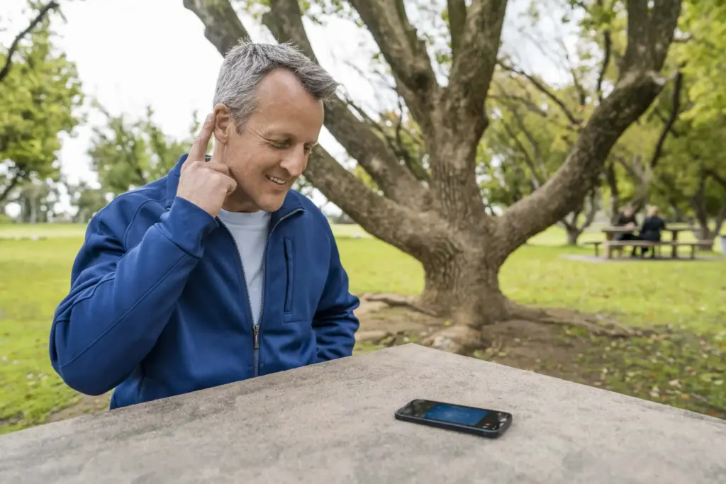 A man taps his in-hear hearing aid to take a call with Bluetooth technology.