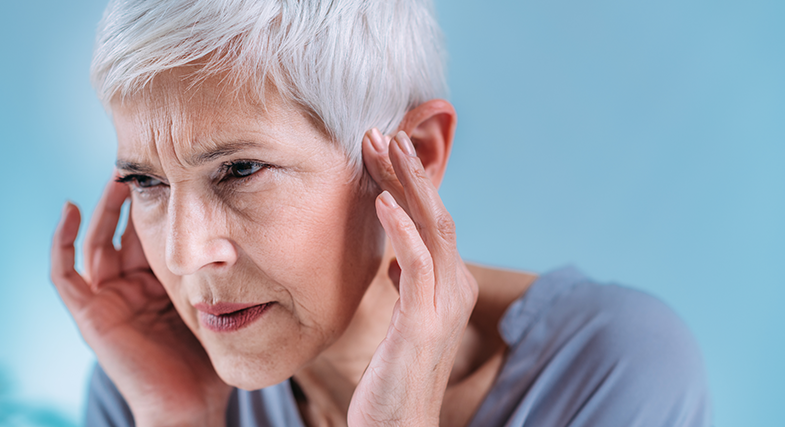 An older woman holds her hands to her temples, experiencing pain and hearing loss.