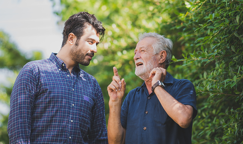 A younger man and older man are pictured having a conversation while on a casual walk outside.