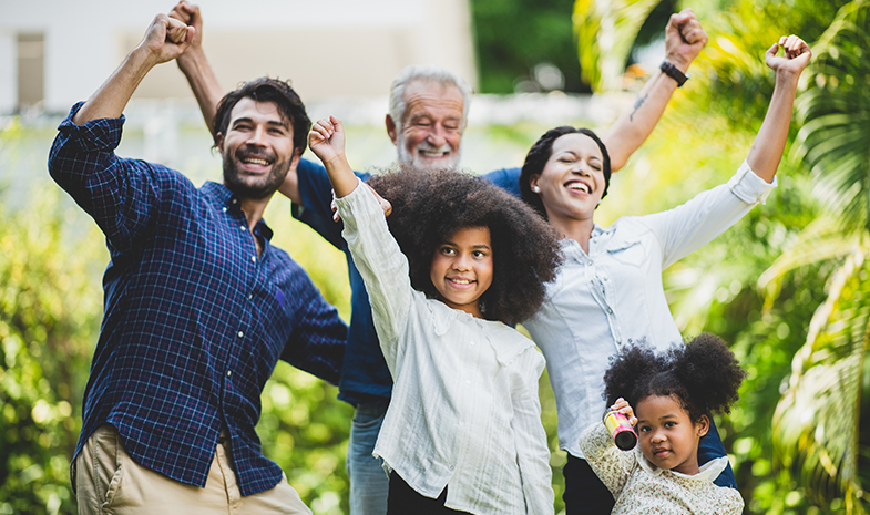 A family dances together outside. The family includes a younger man, older man, a young woman, and two young children.