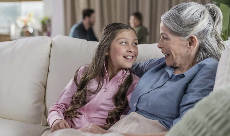 A young girl and an older woman sit side by side on a couch, chatting with each other.